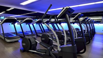 Modern fitness center equipped with treadmills and elliptical machines, under blue lights at Hotel Cascais Miragem