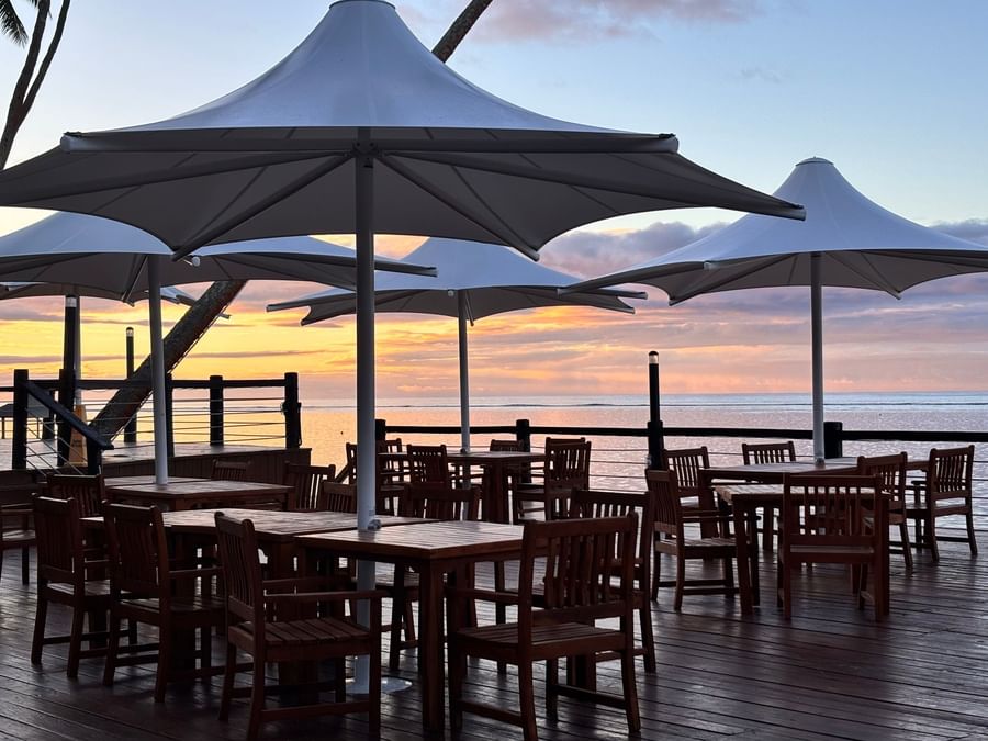 Outdoor wooden tables and chairs under large umbrellas at Warwick Fiji Resort and Spa.