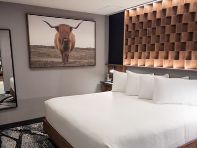 White bed with six pillows and bull picture on wall at Carriage House Hotel & Conference Centre