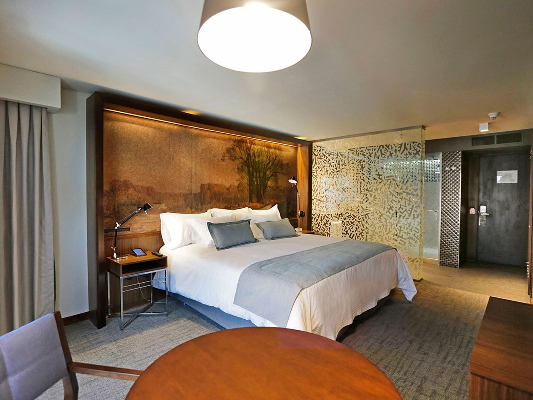 Habitación Doble Superior Matrimonial del Hotel Cumbres Lastarria con cama grande, mesa, silla, cortina, lámpara y baño.