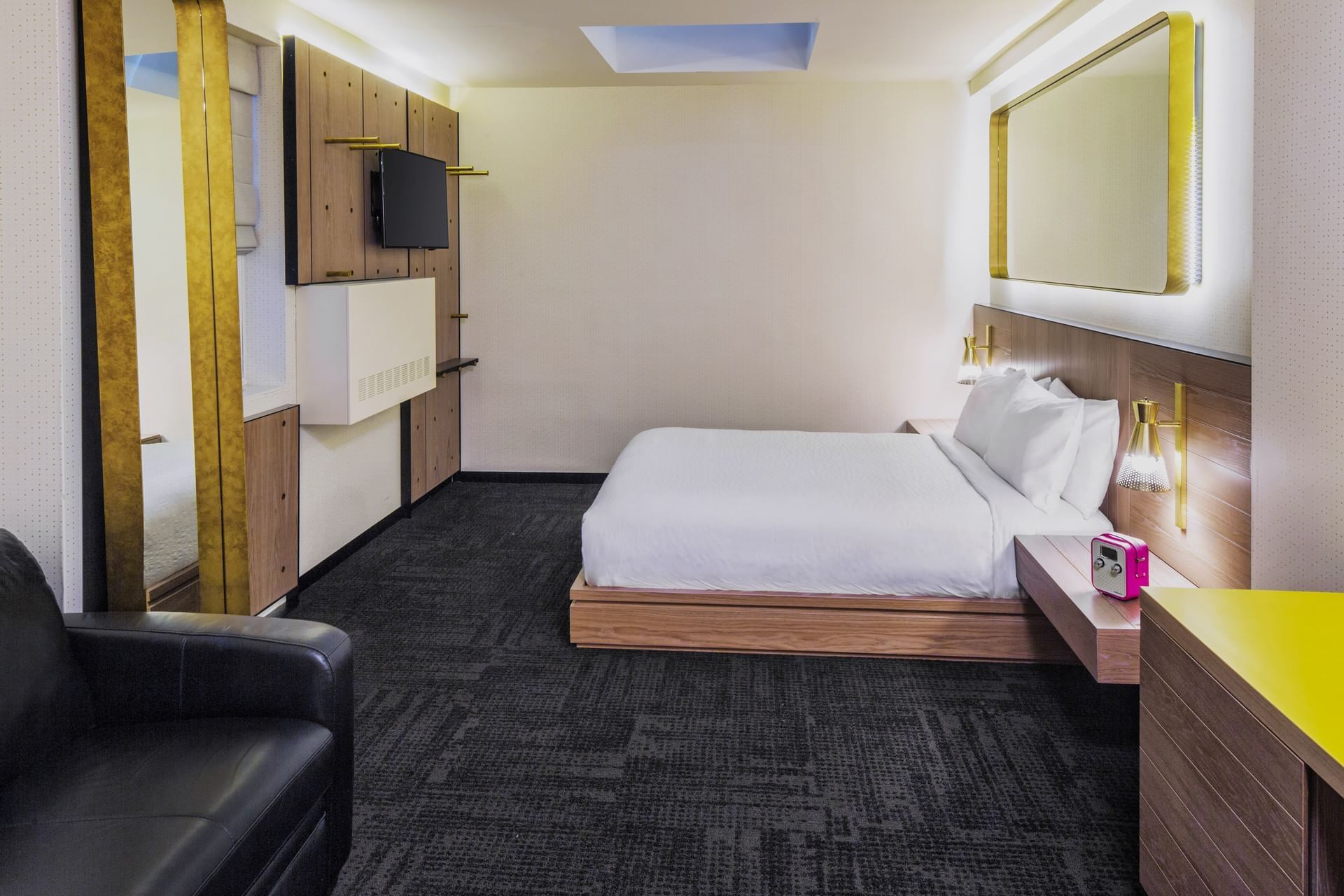 A hotel room with a bed, TV, mirror, sofa, and carpet.