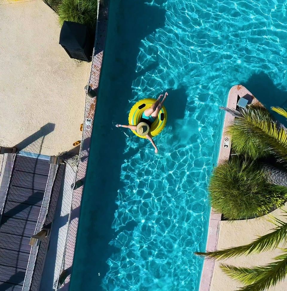 Overhead drone shot of a person relaxing on a yellow tube in the turquoise blue lazy river at Centennial Plaza Resort