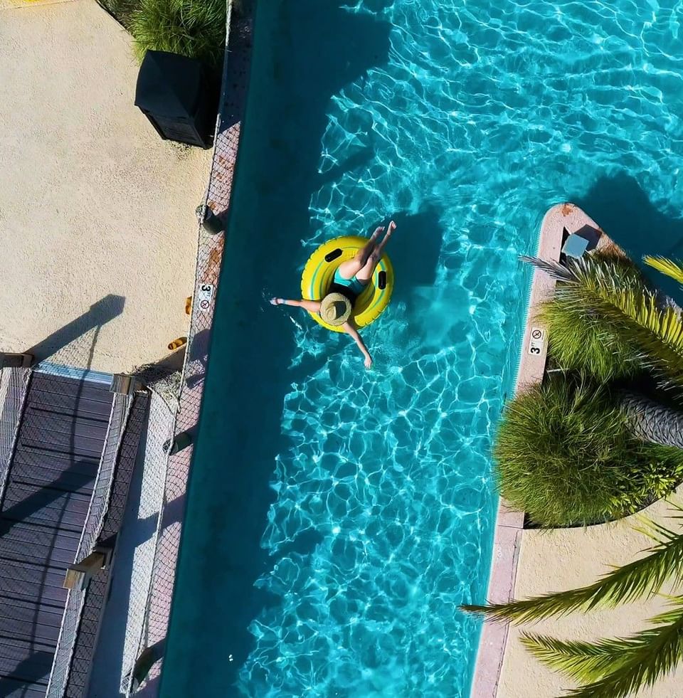 Overhead drone shot of a person relaxing on a yellow tube in the turquoise blue lazy river at Centennial Plaza Resort