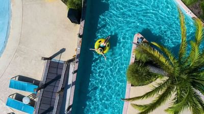 Overhead drone shot of a person relaxing on a yellow tube in the turquoise blue lazy river at Centennial Plaza Resort