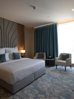 King bed with grey pillows by armchairs under blue curtains in Executive Suite at Cantonal Hotel by Warwick Riyadh