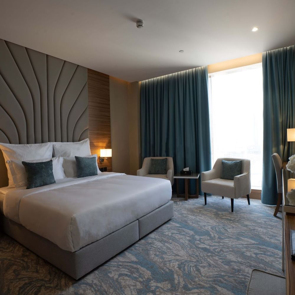 King bed with grey pillows by armchairs under blue curtains in Executive Suite at Cantonal Hotel by Warwick Riyadh