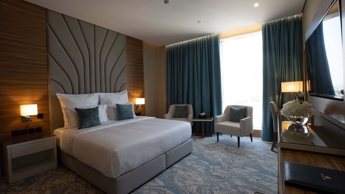 King bed with grey pillows by armchairs under blue curtains in Executive Suite at Cantonal Hotel by Warwick Riyadh