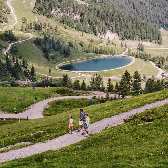 Famiglia di quattro persone che cammina su un sentiero in una zona montuosa con un lago.