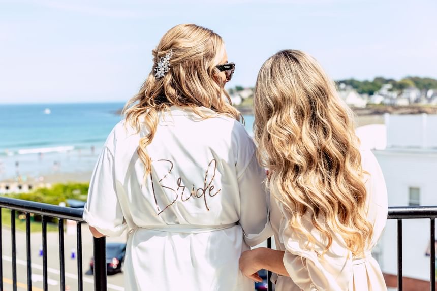 Bride & bridesmaid in robes on the balcony overlooking the sea at Ogunquit Collection