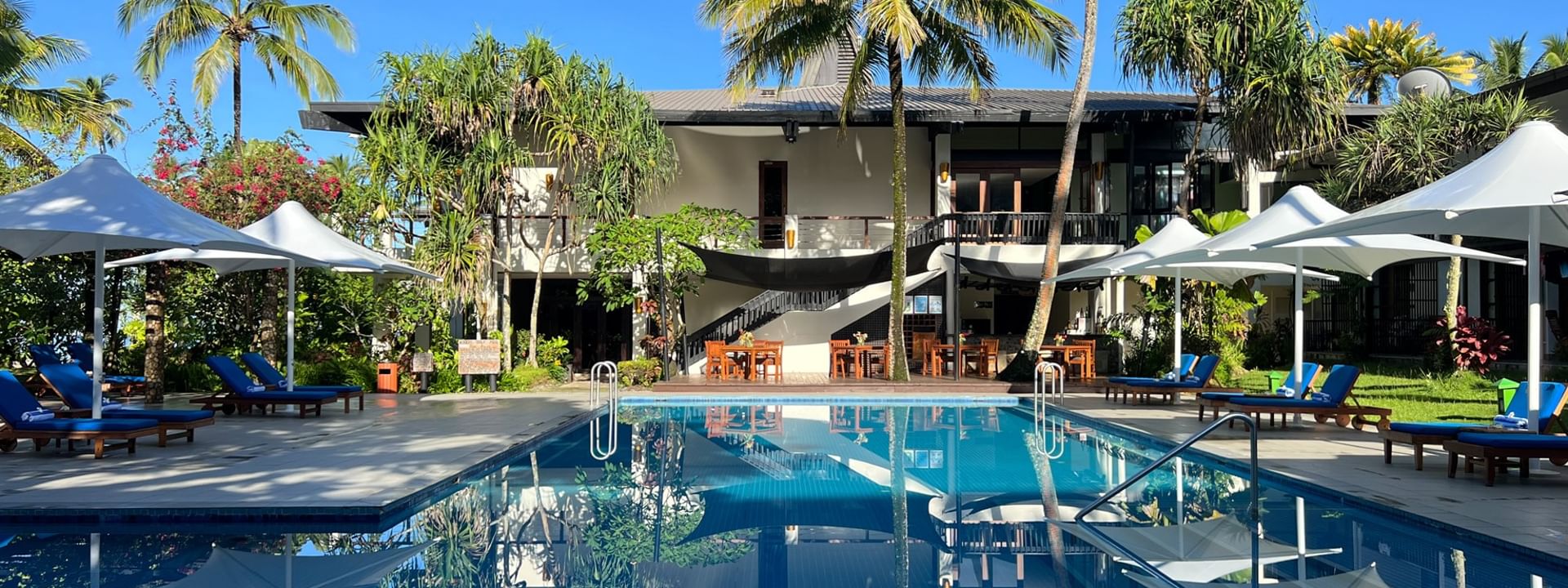 Outdoor pool by white umbrellas and blue lounge chairs at Warwick Fiji Resort and Spa, Korolevu