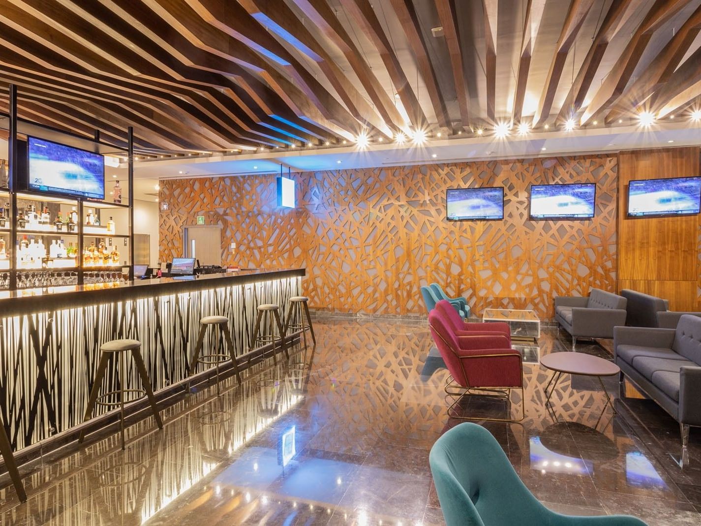 Blue bar with a long illuminated counter, barstools, and multiple TVs at Camino Real Fashion Drive, Monterrey