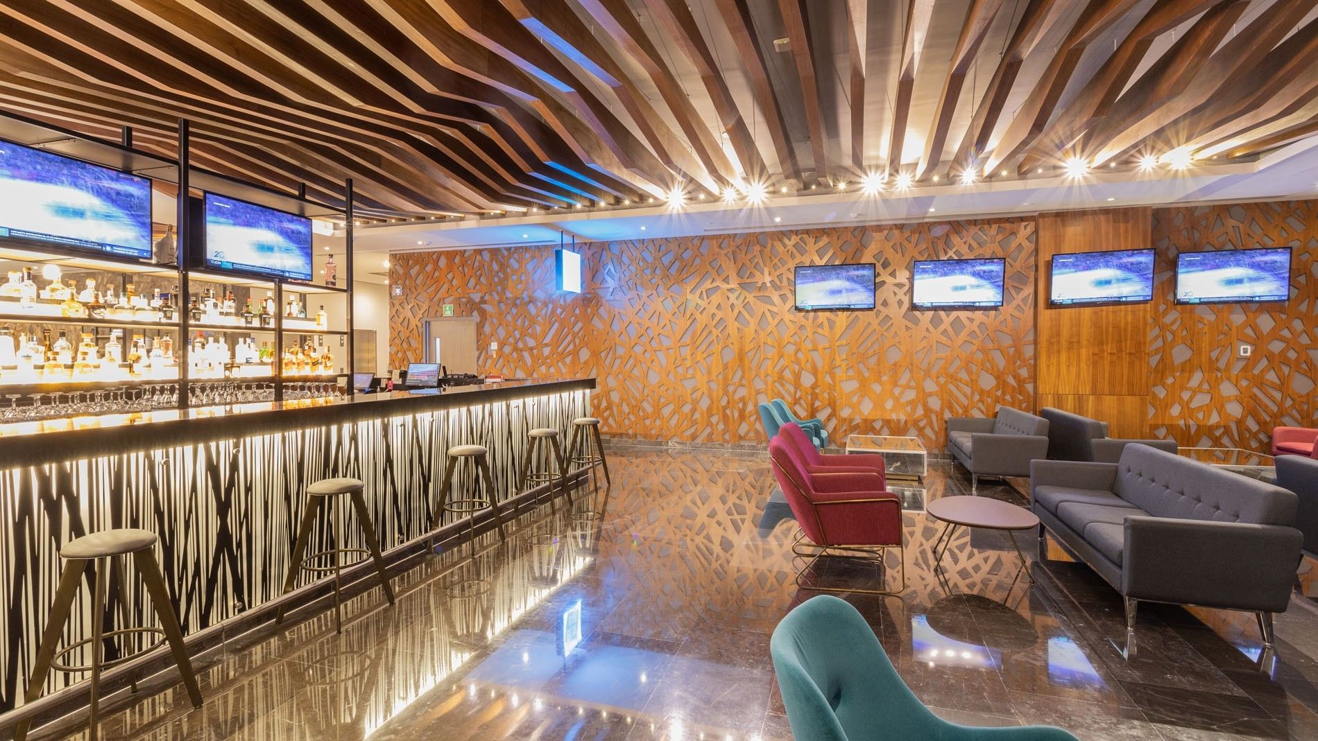 Blue bar with a long illuminated counter, barstools, and multiple TVs at Camino Real Fashion Drive, Monterrey