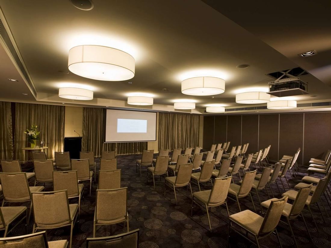 Professional conference room at The Sebel Mandurah with rows of chairs facing a projector screen for business events