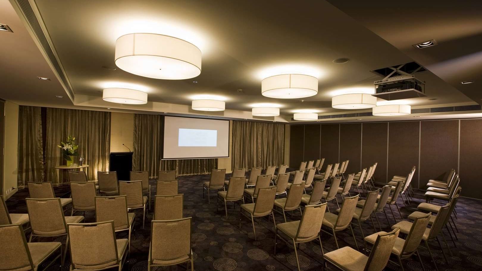 Professional conference room at The Sebel Mandurah with rows of chairs facing a projector screen for business events