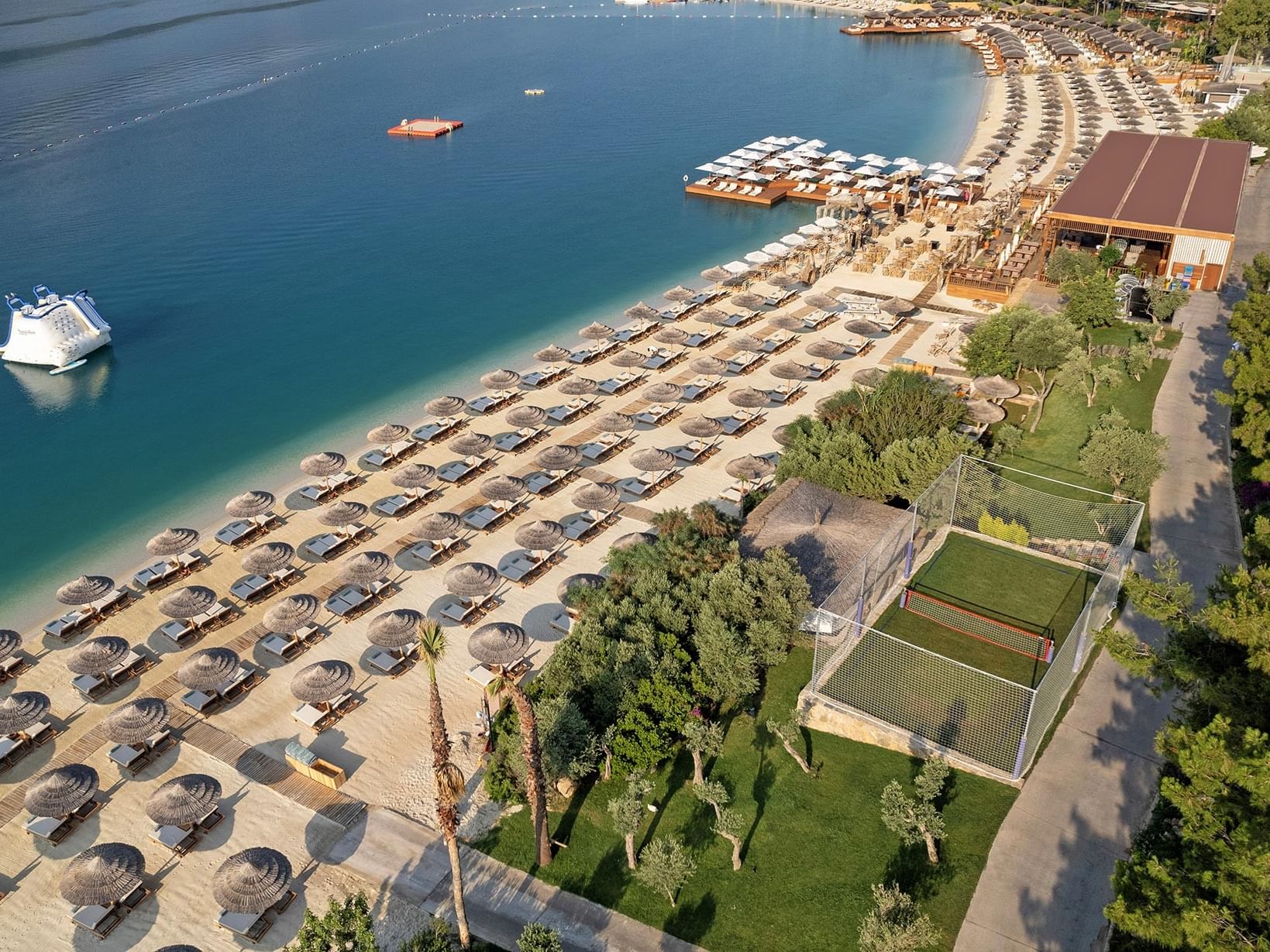 At Titanic Luxury Collection Bodrum, the beach, pool, loungers, umbrellas, and boats by the sea create a captivating aerial view.