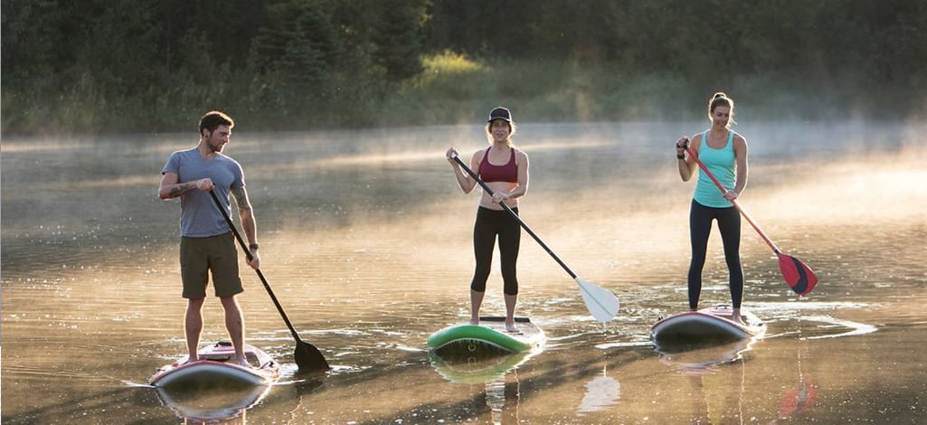 Three people paddle boarding on Alta Lake in Whistler during a misty morning