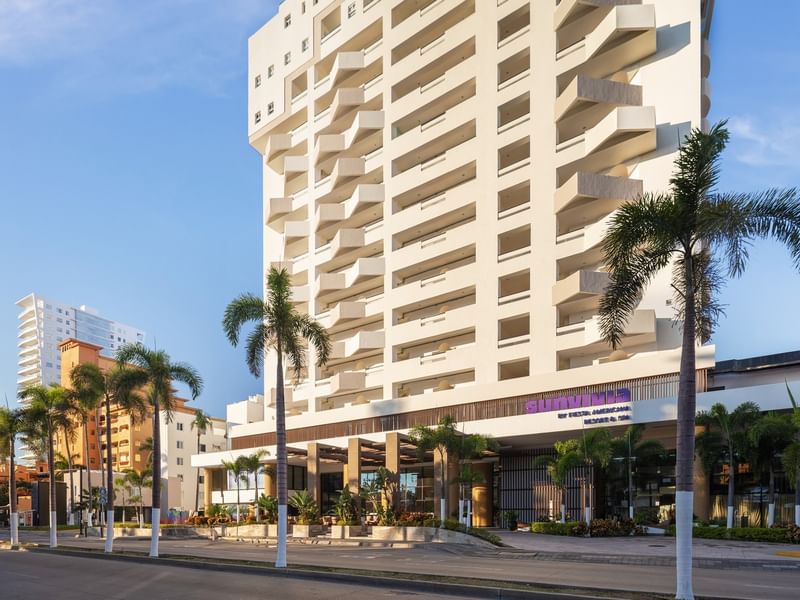 Street-level view of the Sunvivia by Fiesta Americana hotel entrance with palm trees and white balconies
