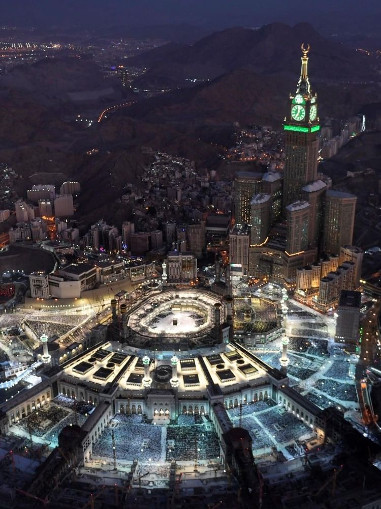 arge mosque with a glowing clock tower by rocky mountains, under a night sky near Warwick Hotels & Resort