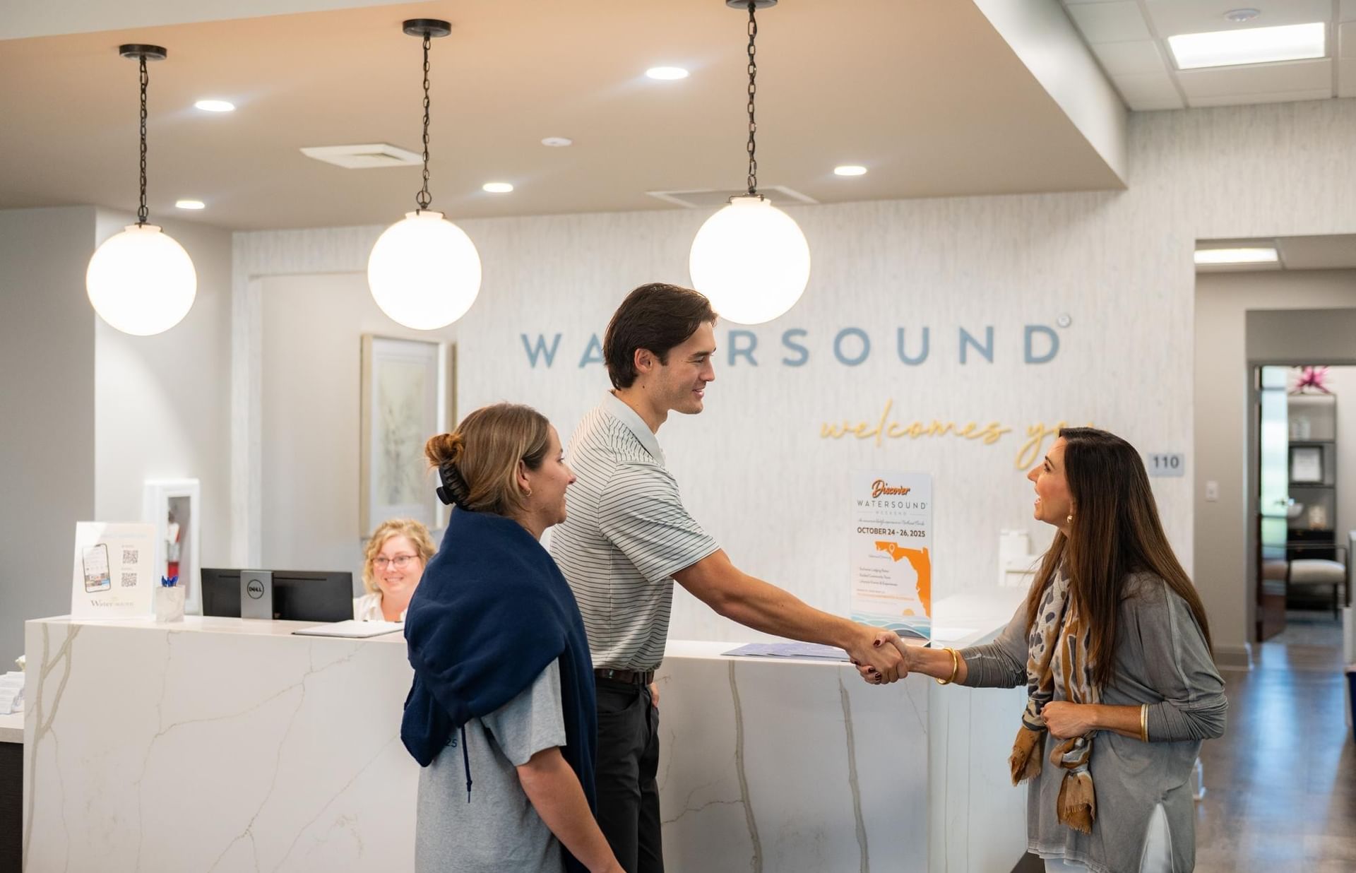 Staff greeting guests with a handshake at a modern reception desk at the Watersound Discovery Center.