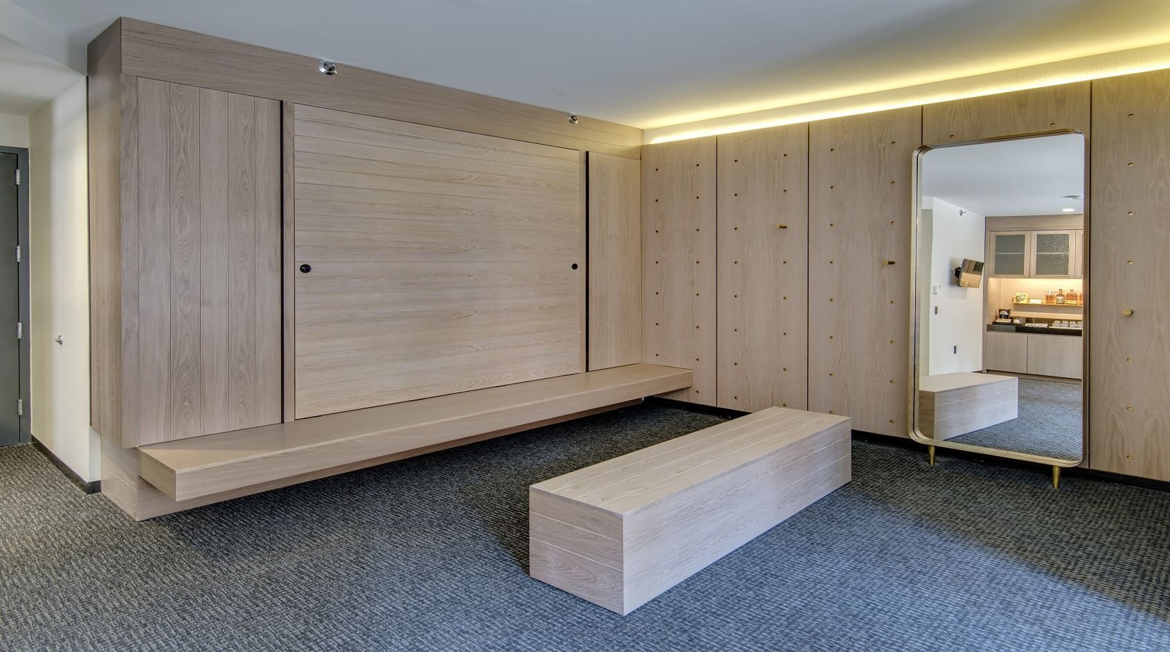 A wide view of a room with wood paneling, a bench, and a mirror.