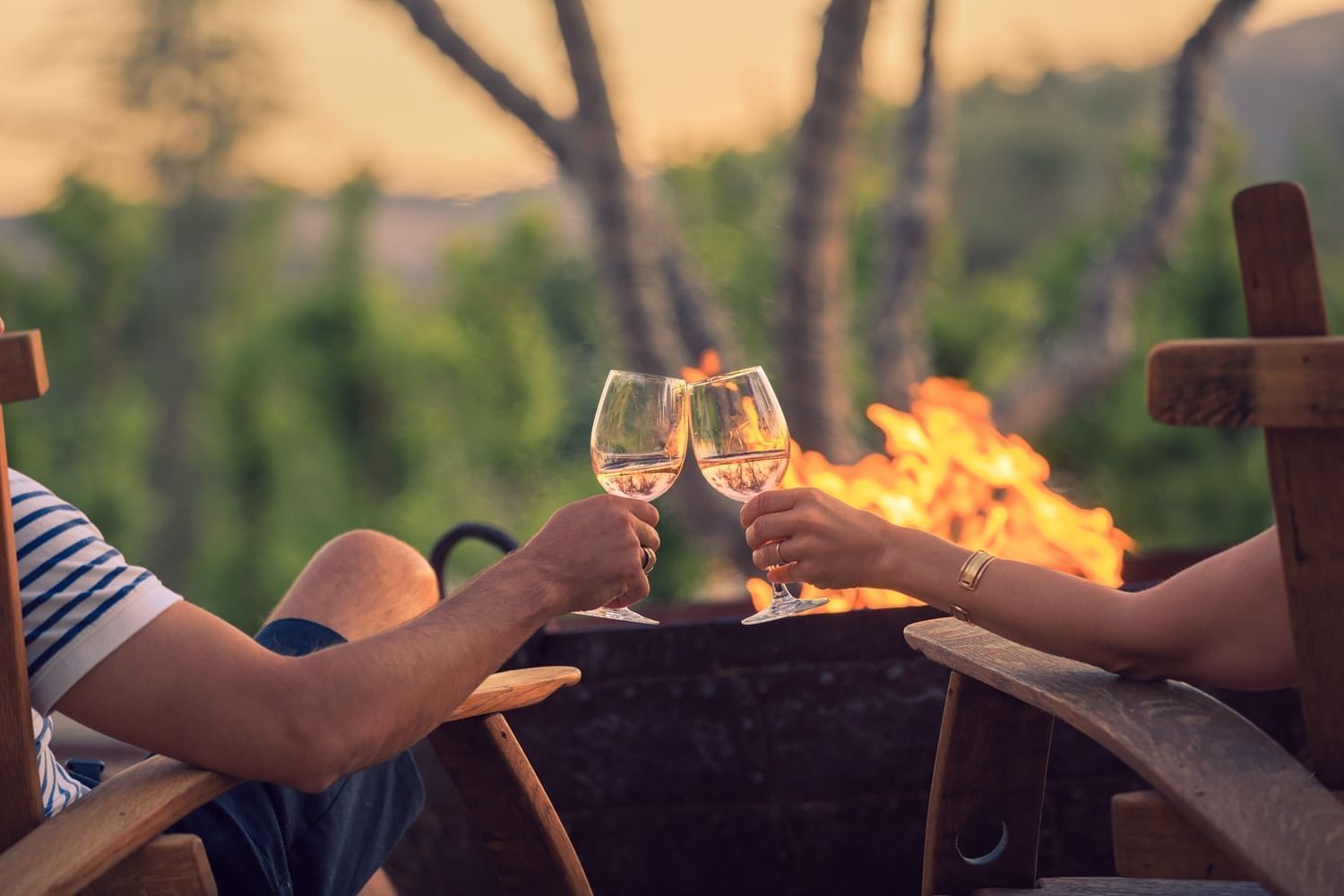 couple holding wine glasses while sitting near firepit
