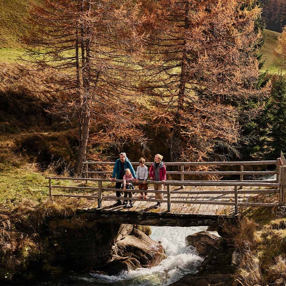 Una famiglia si gode una passeggiata su un ponte di legno sopra un torrente, con alberi sullo sfondo.