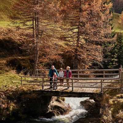 Familie steht auf einer hölzernen Brücke über einem Bach, umgeben von herbstlichen Bäumen.