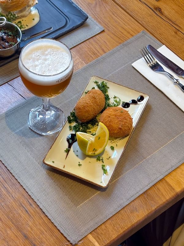 Twee goudbruine kroketten met citroen en peterselie op een bord, geserveerd met een Belgisch bier bij Warwick Brussels