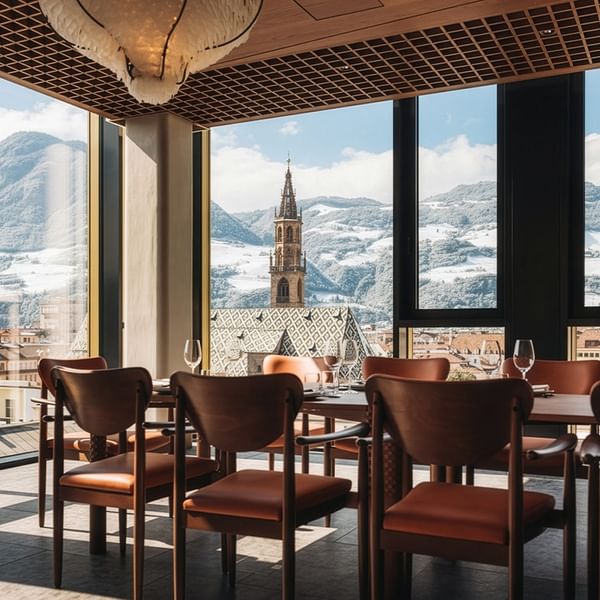 Dining room with large windows, wooden chairs, and a view of a cityscape and mountains.