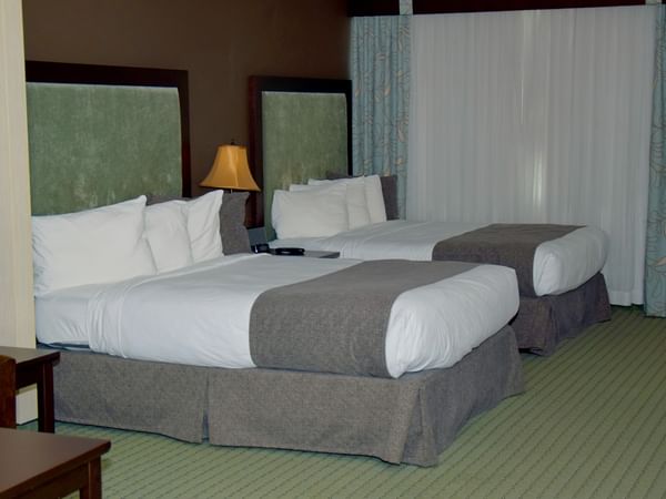 Two beds with white sheets and pillows, curtains, lamps, and furniture in a hotel room.