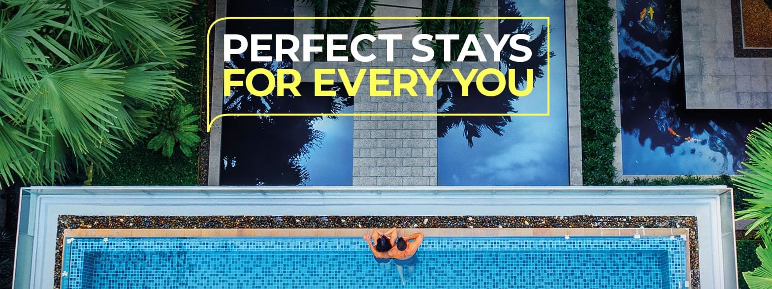 Aerial view of a pool with two people relaxing, surrounded by plants and buildings.