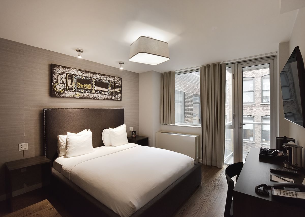 A hotel room with a queen bed, desk, flat-screen TV, and balcony access.