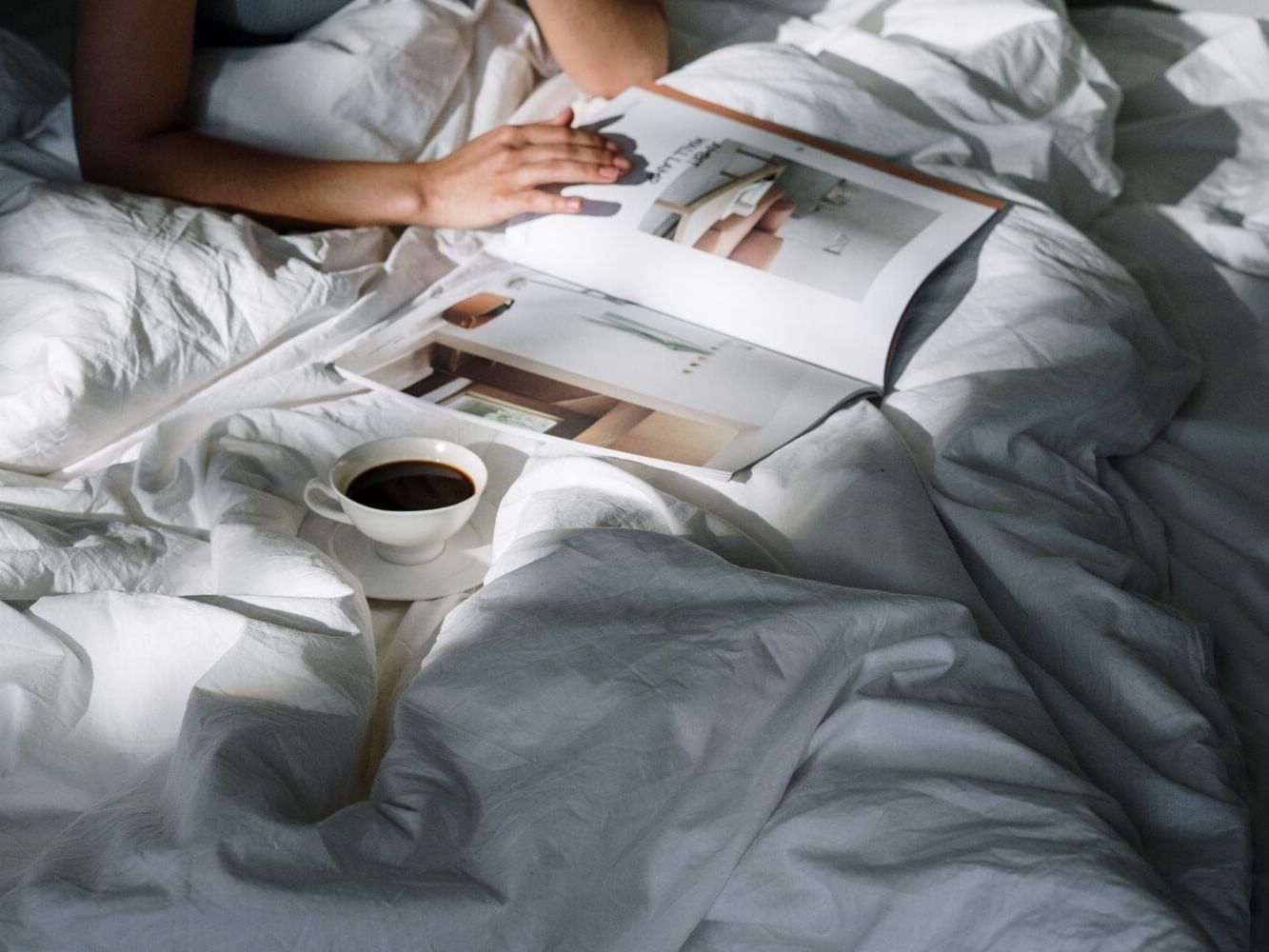 A lady reading a magazine on bed with a coffee at Amora Hotel