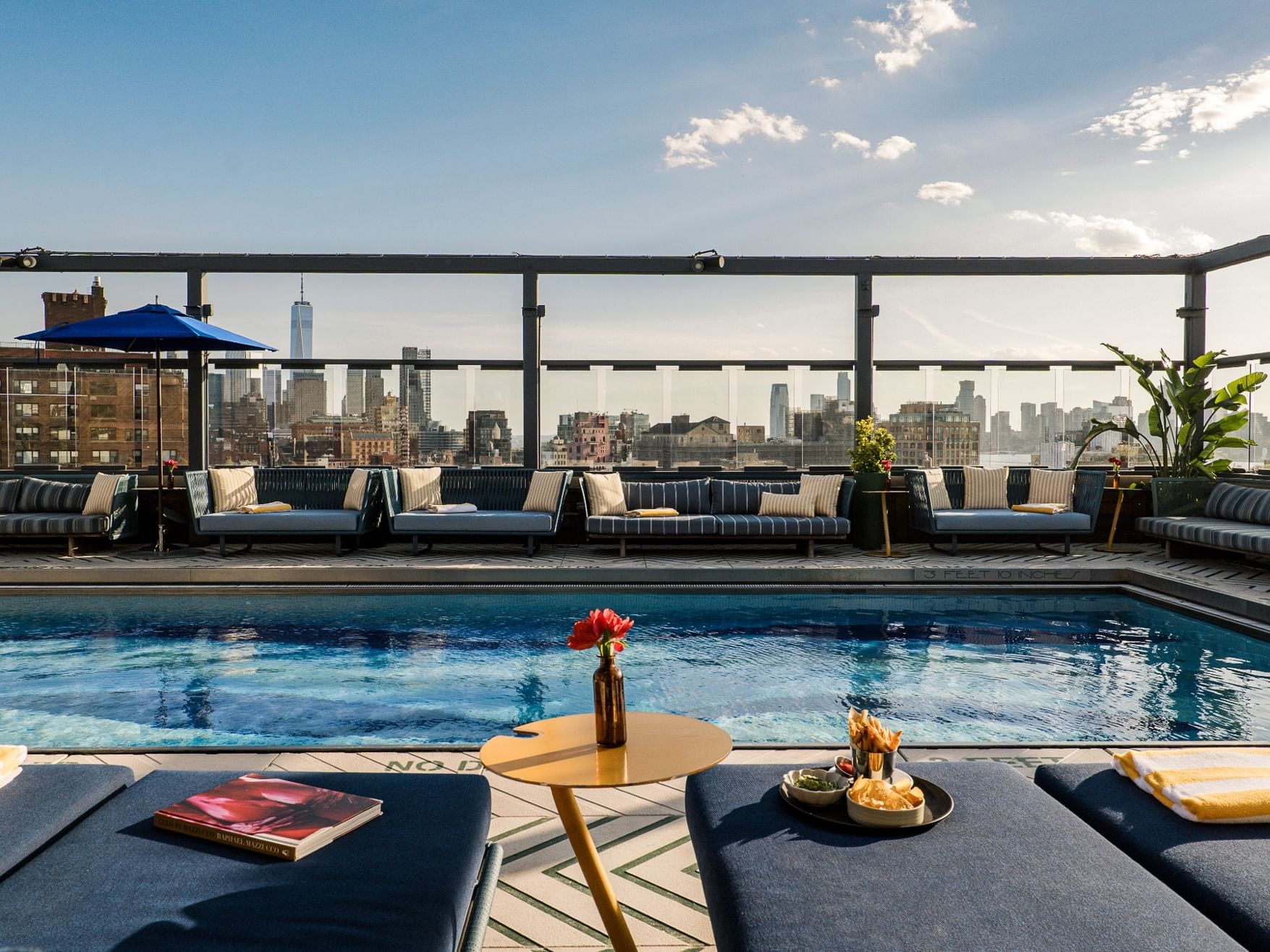 Rooftop pool with lounge seating and city skyline views under a bright summer sky for Summer Stay offer.