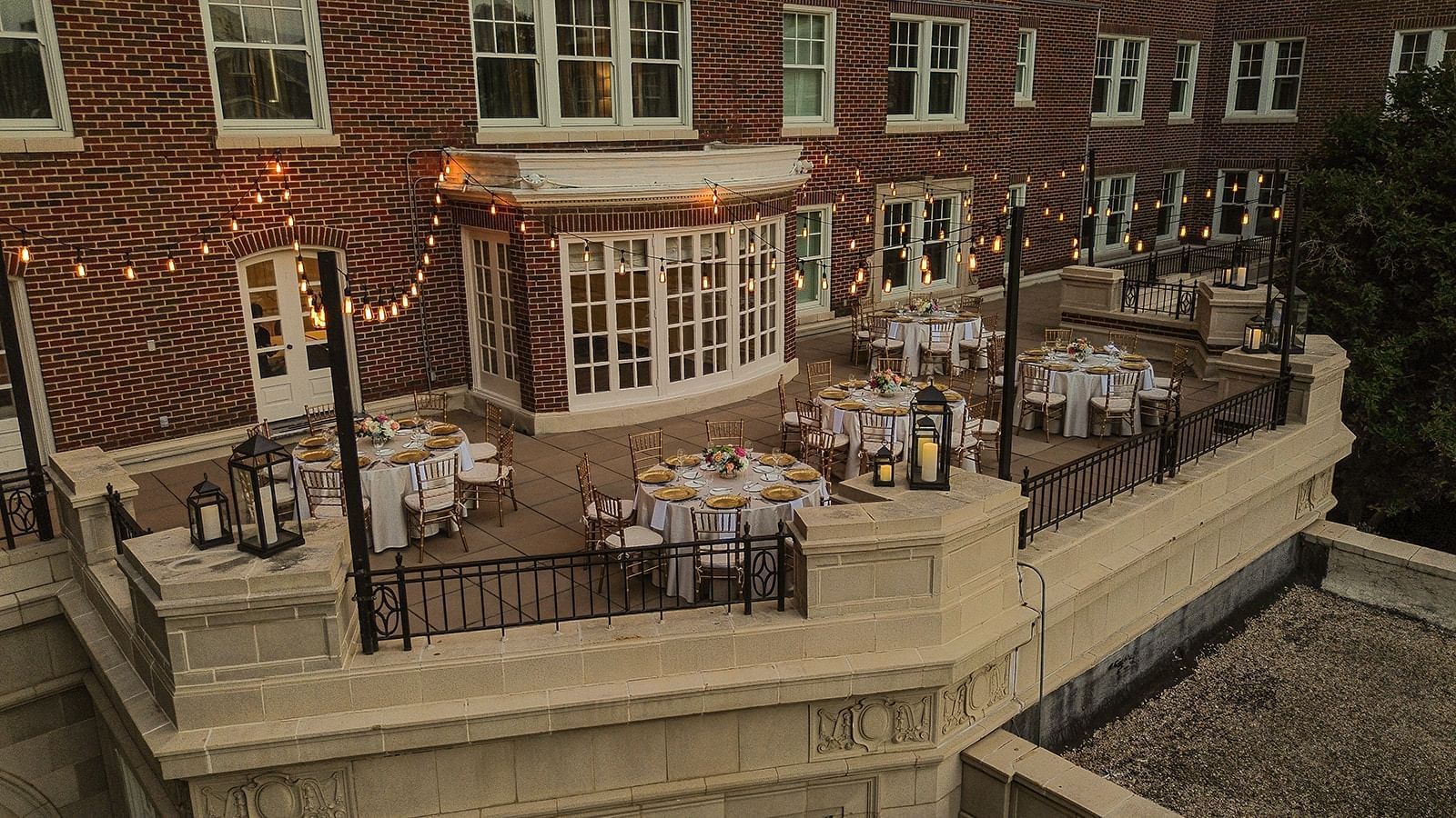 View of The Bridewell Suite with Round tables by string lights under a brick facade at Warwick Melrose Dallas