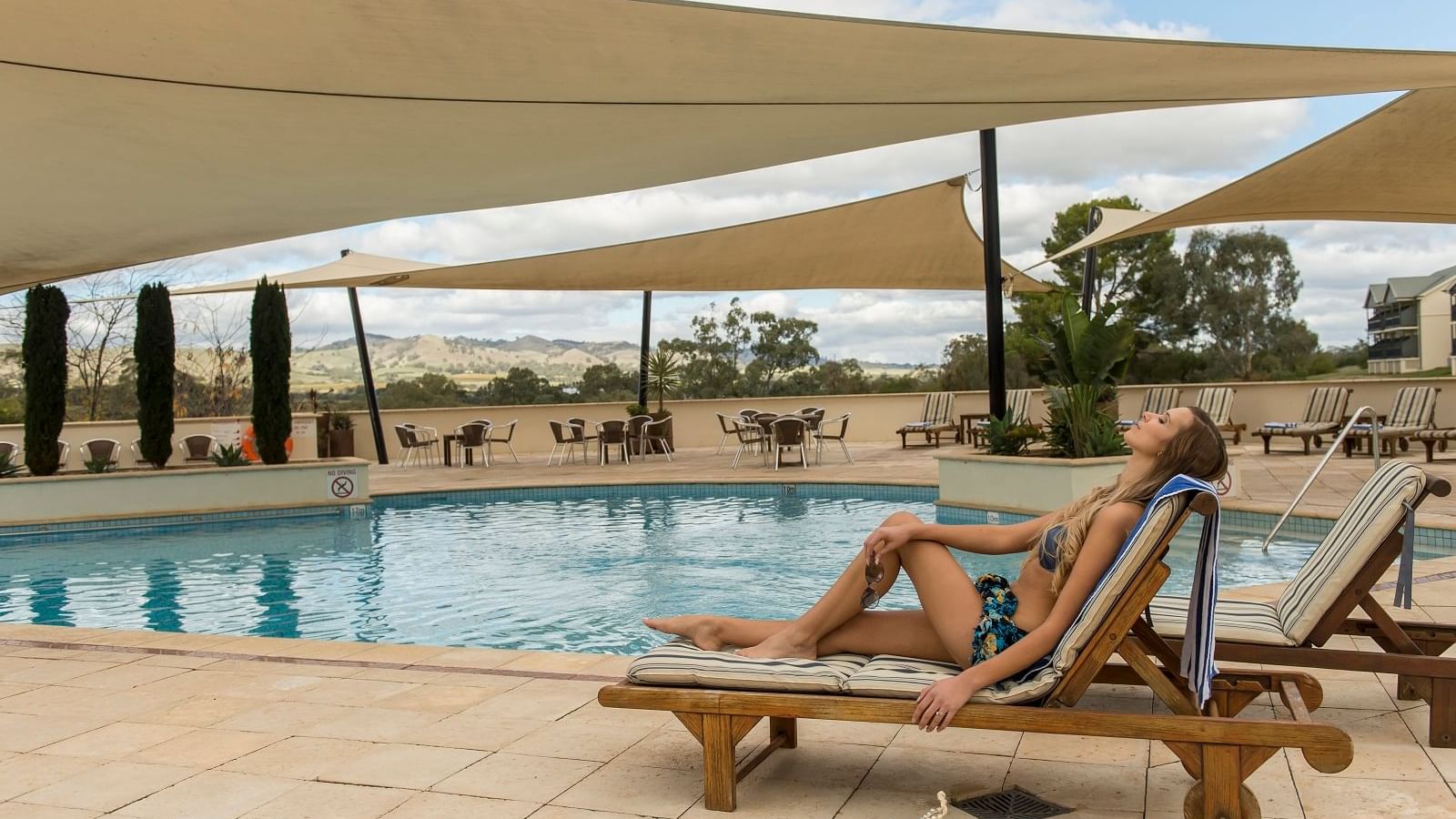 A lady relaxing in lounge chairs by the pool at Novotel Barossa