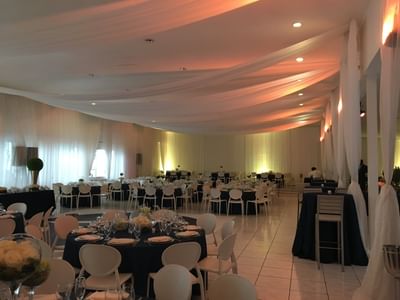 Round tables with navy linens under draped white ceiling and warm lighting in Frank Room & Terrace at Hotel Montana Haiti