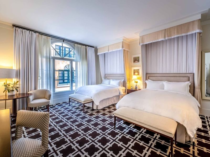 Sitting area and ottomans by the cozy beds in Deluxe Queen Mobility and Hearing Accessible at El Prado Hotel