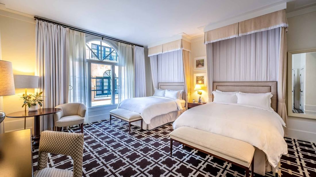 Sitting area and ottomans by the cozy beds in Deluxe Queen Mobility and Hearing Accessible at El Prado Hotel