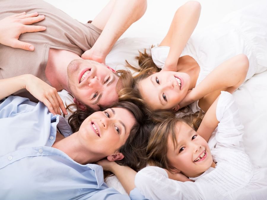 Une famille de quatre personnes allongée sur un lit, dans le cadre de l'offre « Family Friendly Hotel » de l'Hôtel Westminster - Paris