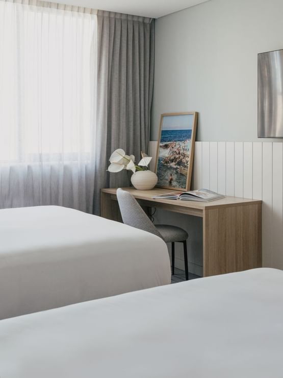 Village Twin at Elysium Manly by a wooden desk with white flowers near a wall TV, offering cozy Manly accommodation