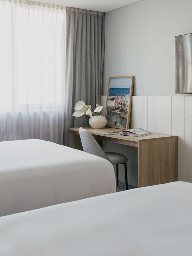 Village Twin at Elysium Manly by a wooden desk with white flowers near a wall TV, offering cozy Manly accommodation