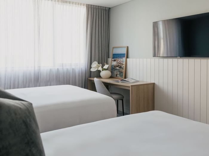 Village Twin at Elysium Manly by a wooden desk with white flowers near a wall TV, offering cozy Manly accommodation
