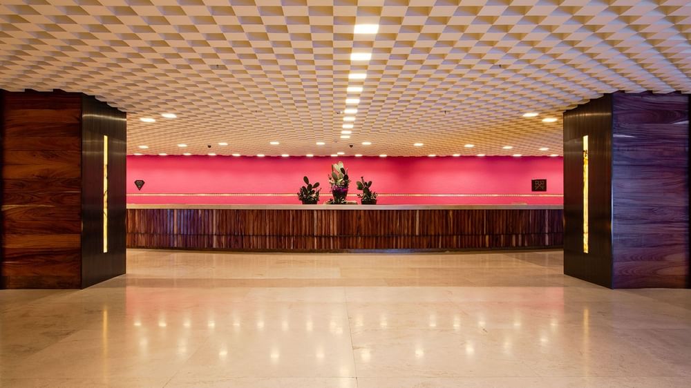 Striking reception desk with a vibrant pink wall and a unique textured ceiling at Camino Real Polanco Mexico