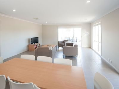 A living area with a dining table, sofa, and television at La Trobe University Regional Housing – Shepparton.