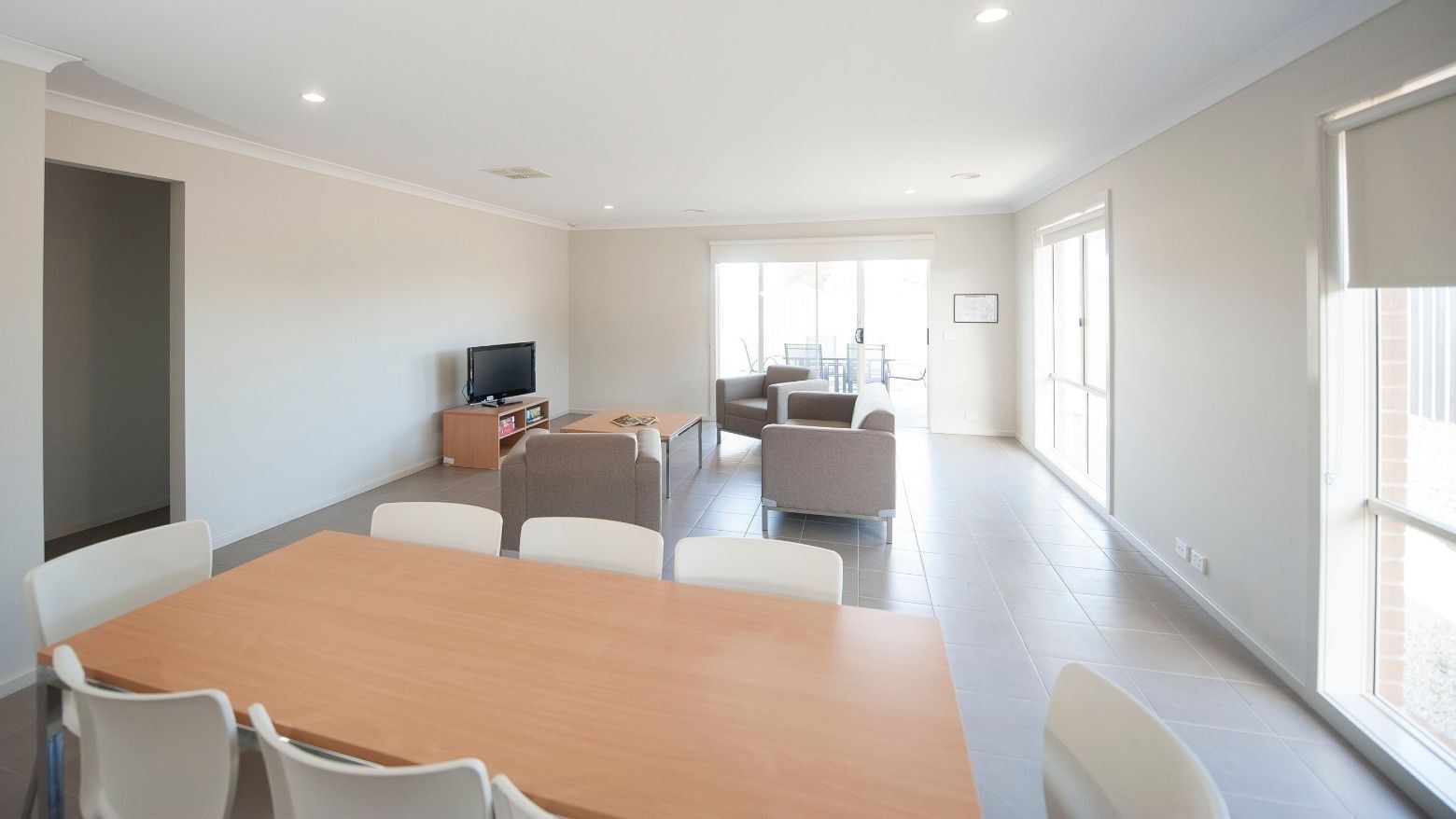 A living area with a dining table, sofa, and television at La Trobe University Regional Housing – Shepparton.