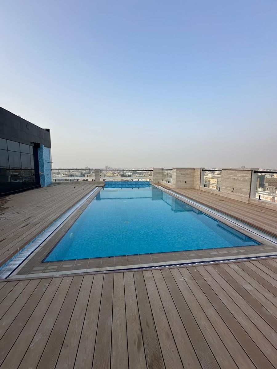 Blue rooftop swimming pool by a wooden deck under a clear sky with city views at Warwick Jeddah Hotel & Spa