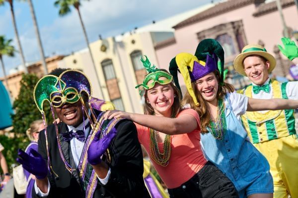 A group of four people in a conga line wearing Mardi Gras inspired accessories. St. Patrick's Day at Universal Orlando Resort celebrates both holidays in one. 