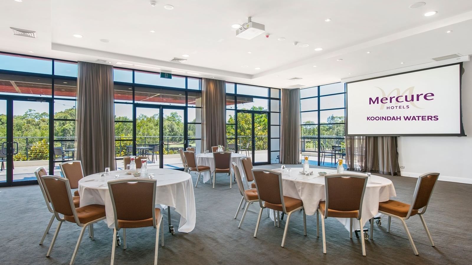 Kooindah Three conference room with tables, chairs, and large windows overlooking trees at Mercure Kooindah Waters