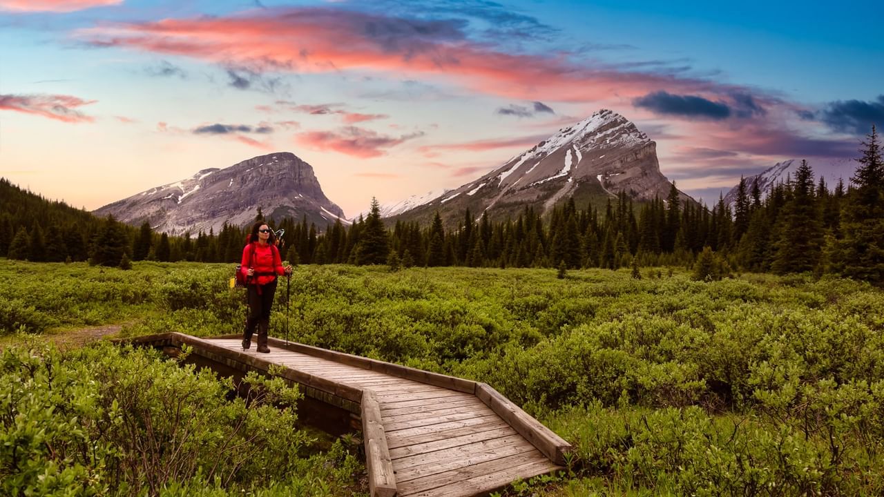 A hiker in a red jacket exploring a scenic mountain trail at sunset.